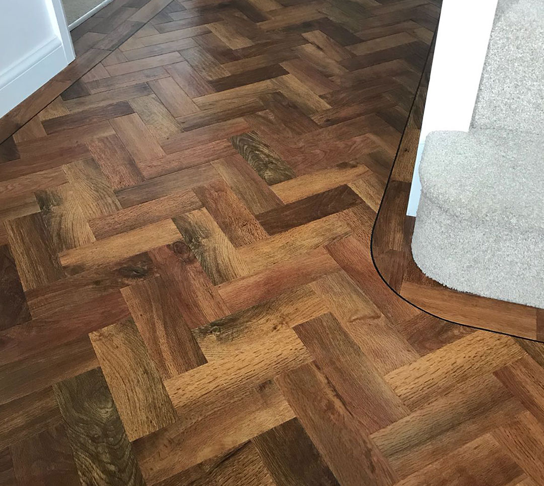 Herringbone wood-effect floor meeting a carpeted stair in a hallway