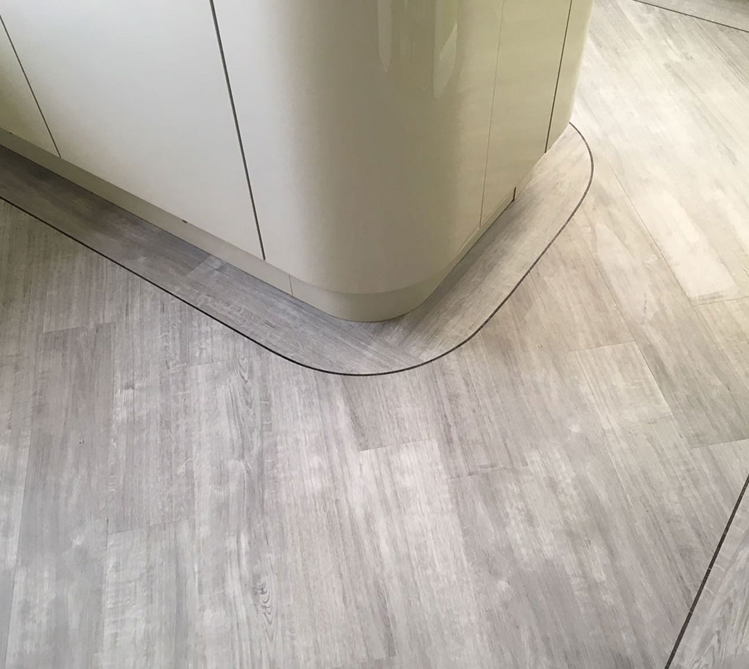 Wood-effect planks cut around a curved kitchen unit with a dark feature strip
